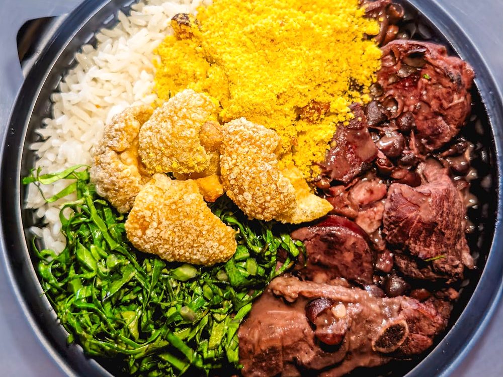 Feijoada na tigela preta, com arroz, farofa, torresmo, couve e carnes, vista de cima