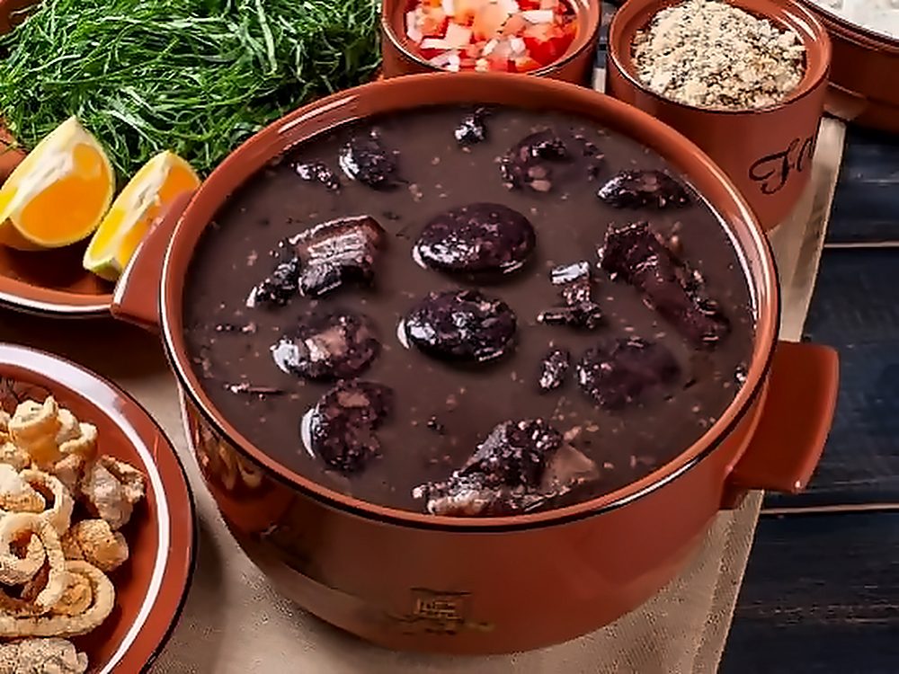 Feijoada na panela de barro, com torresmo, laranja, vinagrete e couve ao lado