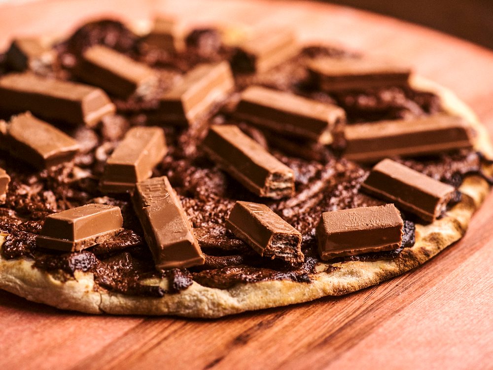 Pizza doce coberta de chocolate e pedaços de KitKat, em close