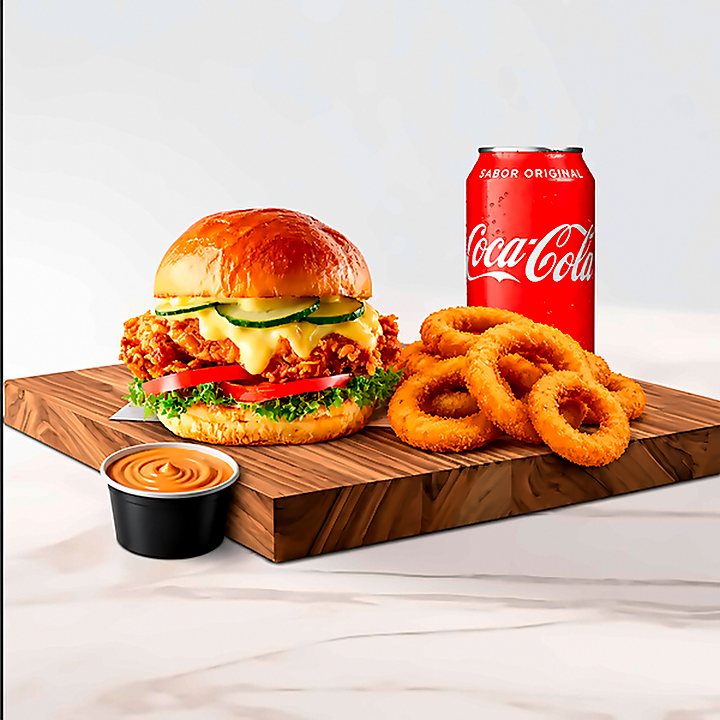 Combo com sanduíche de frango empanado com cheddar derretido, anéis de cebola, lata de Coca-Cola e pote de molho, sobre tábua de madeira